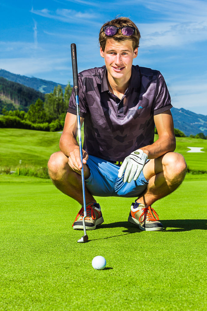 Mann in Hocke mit Golfschläger und Ball auf dem Grün