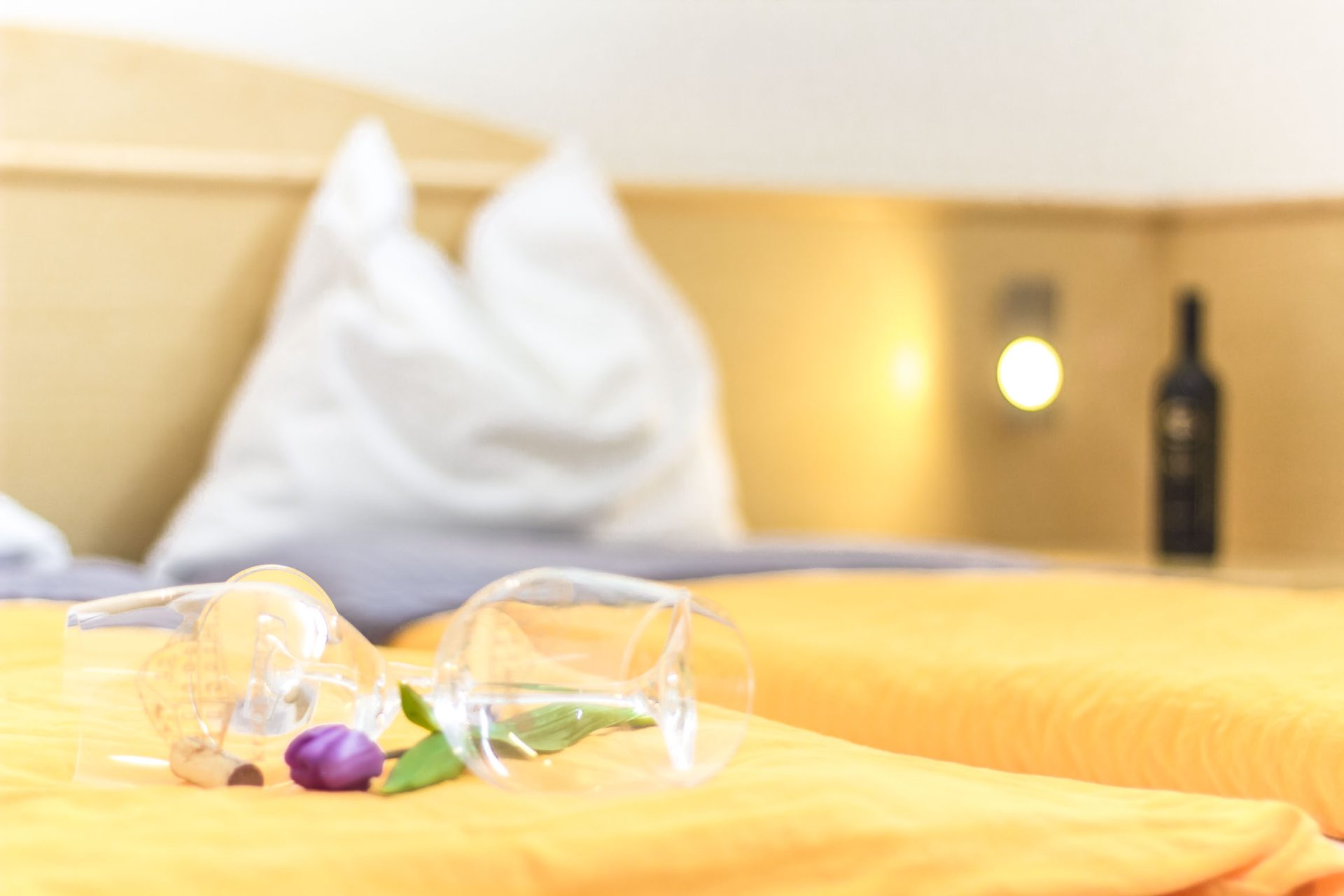 Bett mit gelber Decke, Weinglass und violetter Tulpe